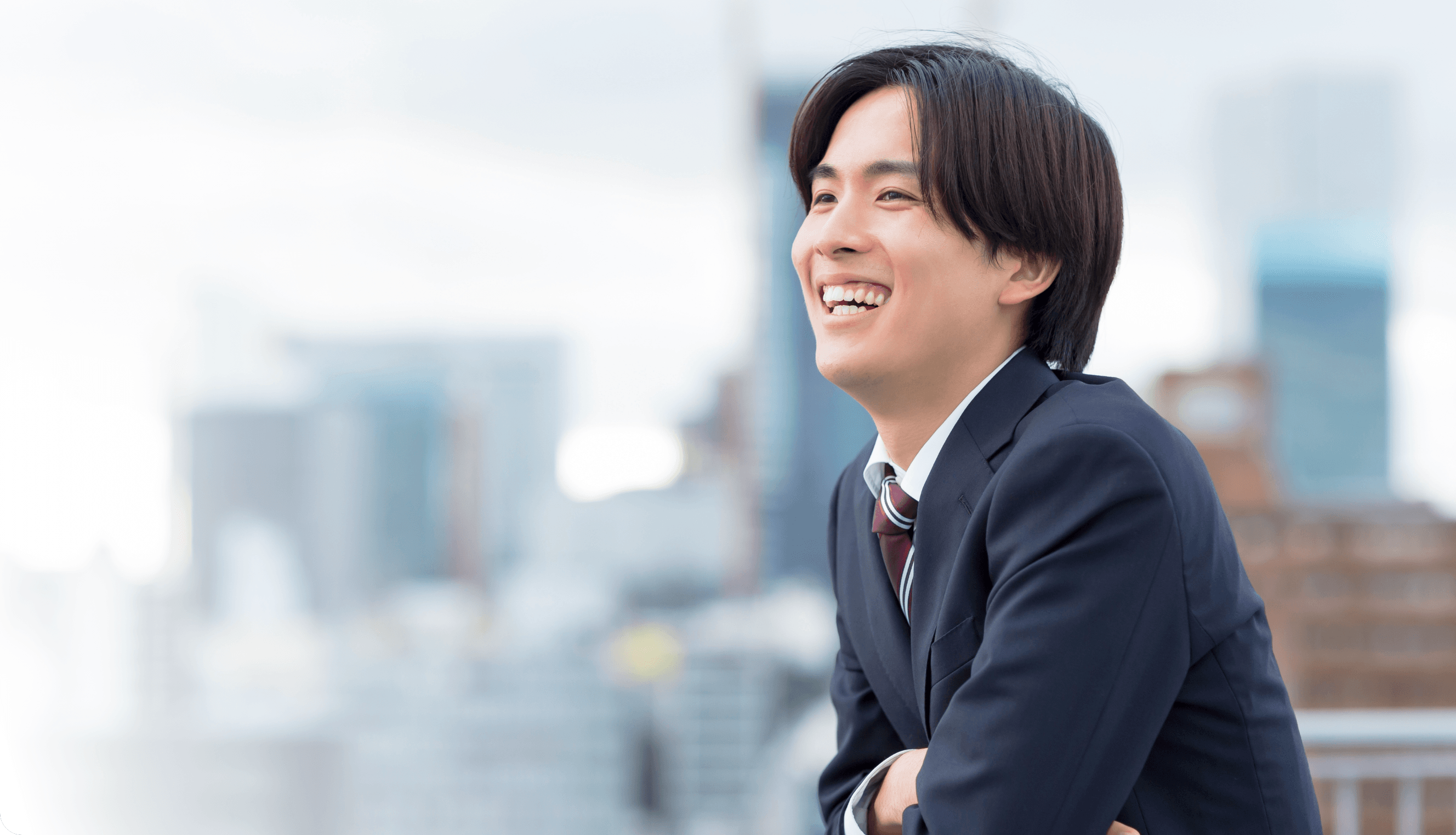 学生服で笑顔の若い男性が外でもたれかかっている様子